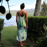 Woman in a floral dress standing in a lush garden with a scenic view of water and mountains.