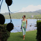 Woman in a floral dress standing by a scenic waterfront with mountains in the background