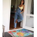 Woman in denim overalls and yellow top standing on a colorful doormat.