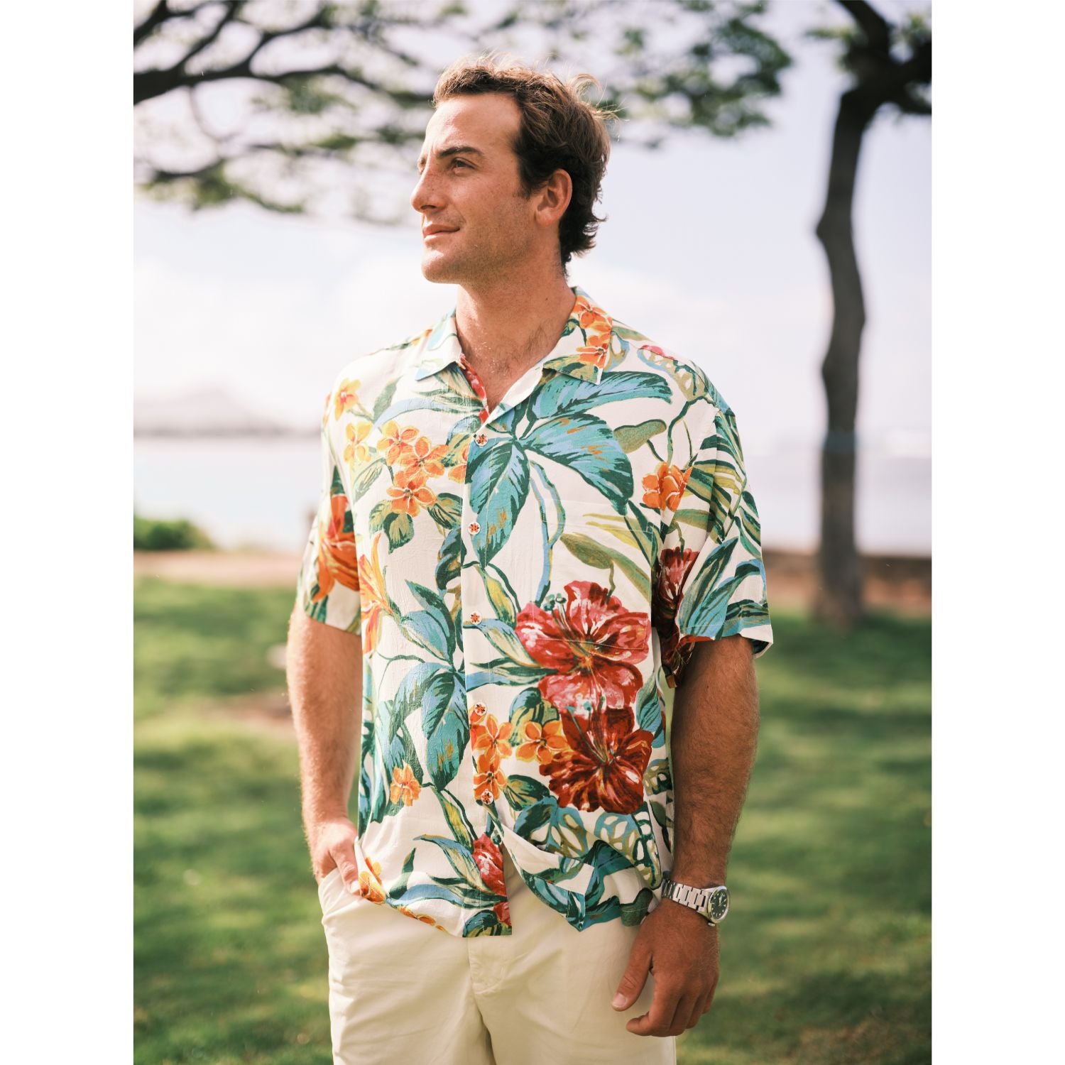 Man wearing a colorful floral shirt standing outdoors with trees and grass in the background