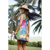 Woman in a colorful dress and hat standing in a tropical setting with palm trees.