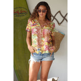 Woman wearing a colorful shirt and denim shorts standing next to a surfboard with 'Surf Line Hawaii' branding.