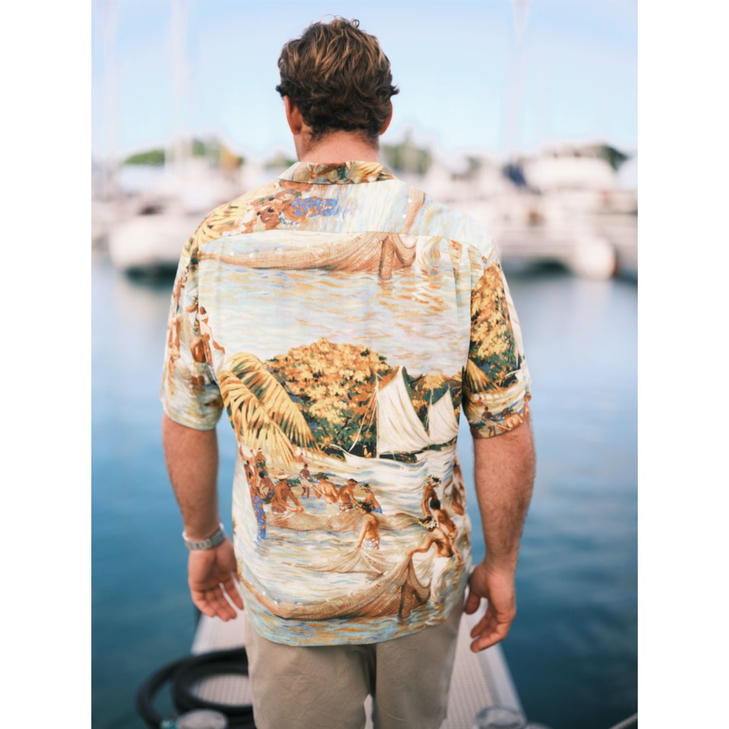 Scenic net fishing scene in the islands button down aloha shirt on model standing on pier.