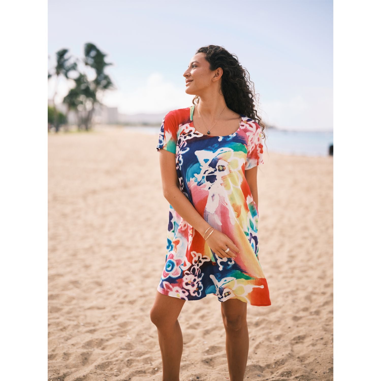 Woman in a colorful dress standing on a beach with palm trees in the background