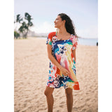 Woman in a colorful dress standing on a beach with palm trees in the background