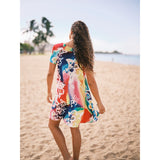 Woman in a colorful dress walking on a sandy beach with palm trees in the background