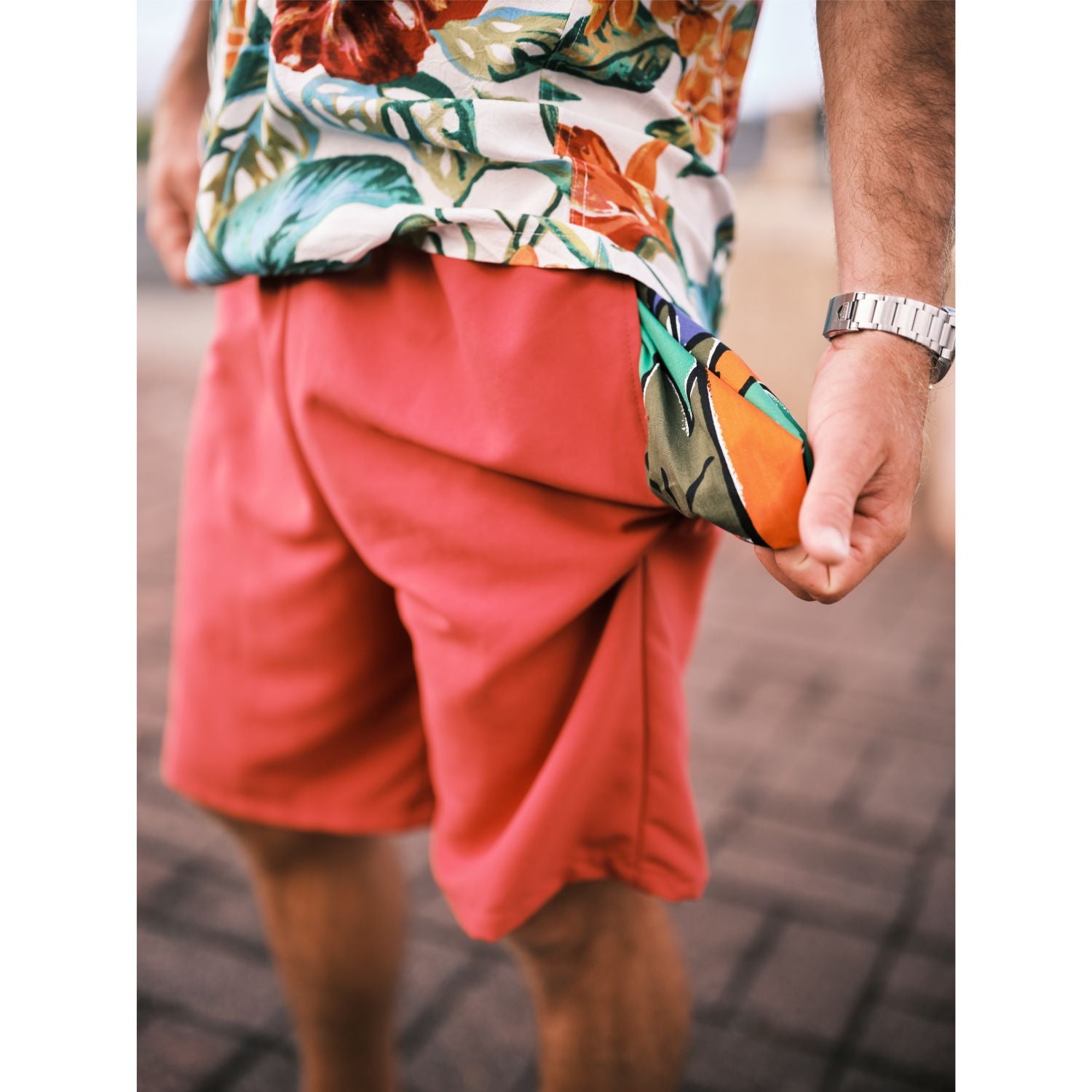Model standing on walk way with solid red shorts pocket pulled out which is in a colorful print.
