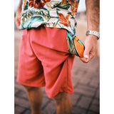Model standing on walk way with solid red shorts pocket pulled out which is in a colorful print.