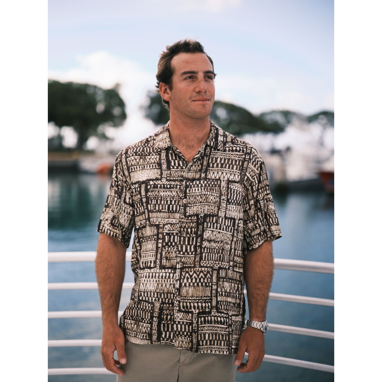 Hombre con camisa estampada de pie en un barco atracado en el muelle.