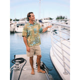 Model wearing Fern Patch button down Aloha shirt, an Abstract art with teal, orange, and green brush strokes. solid Khaki shorts standing on pier.