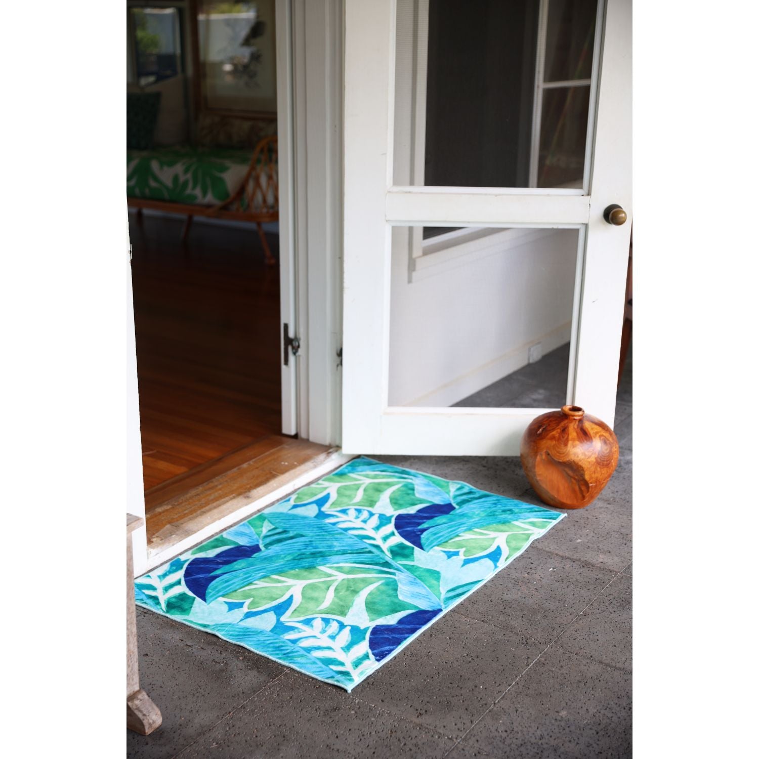 Alfombra con estampado de hojas tropicales en colores azul y verde colocada fuera de la puerta.