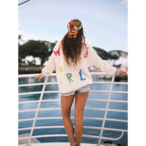Model wearing a colorful 'JAMS WORLD' sweater on a boat deck with water and trees in the background