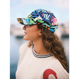 Modelo de pie en el muelle, con gorra Reef de estampado de peces coloridos y el logo de Jams World, suéter vintage y pantalones cortos vaqueros.