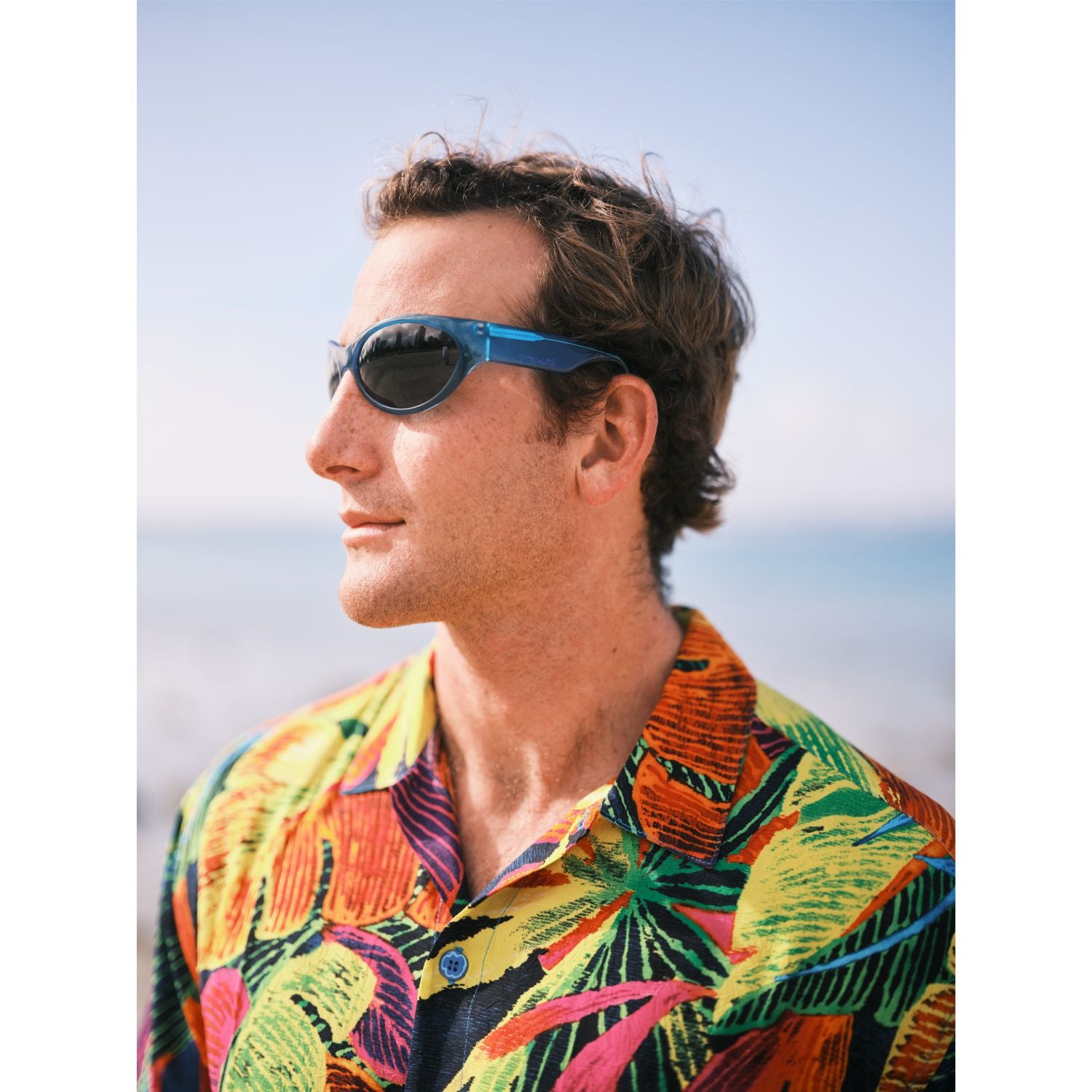 Man wearing sunglasses and a patterned shirt with a blurred background