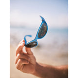 Hand holding blue sunglasses with case and blurred beach background