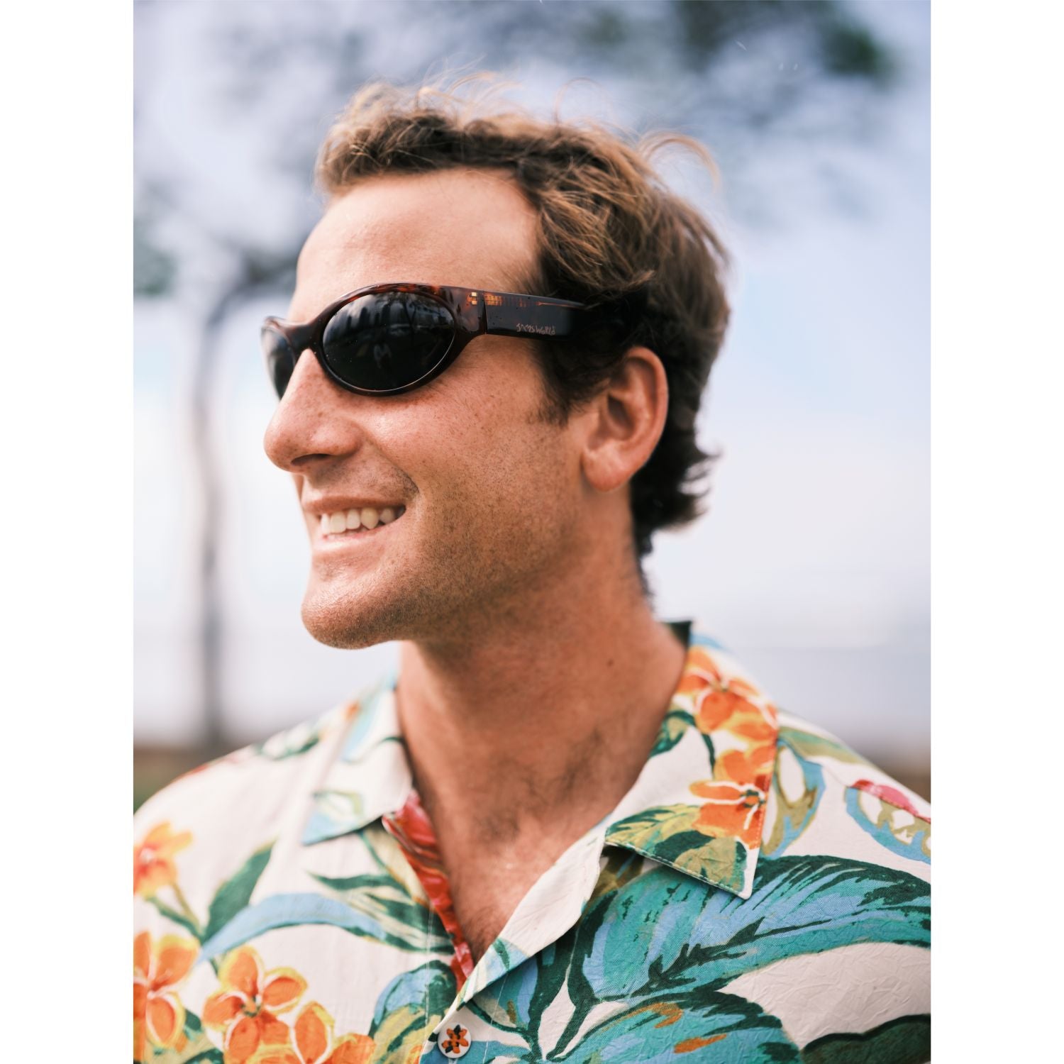 Hombre con gafas de sol y camisa estampada con fondo borroso