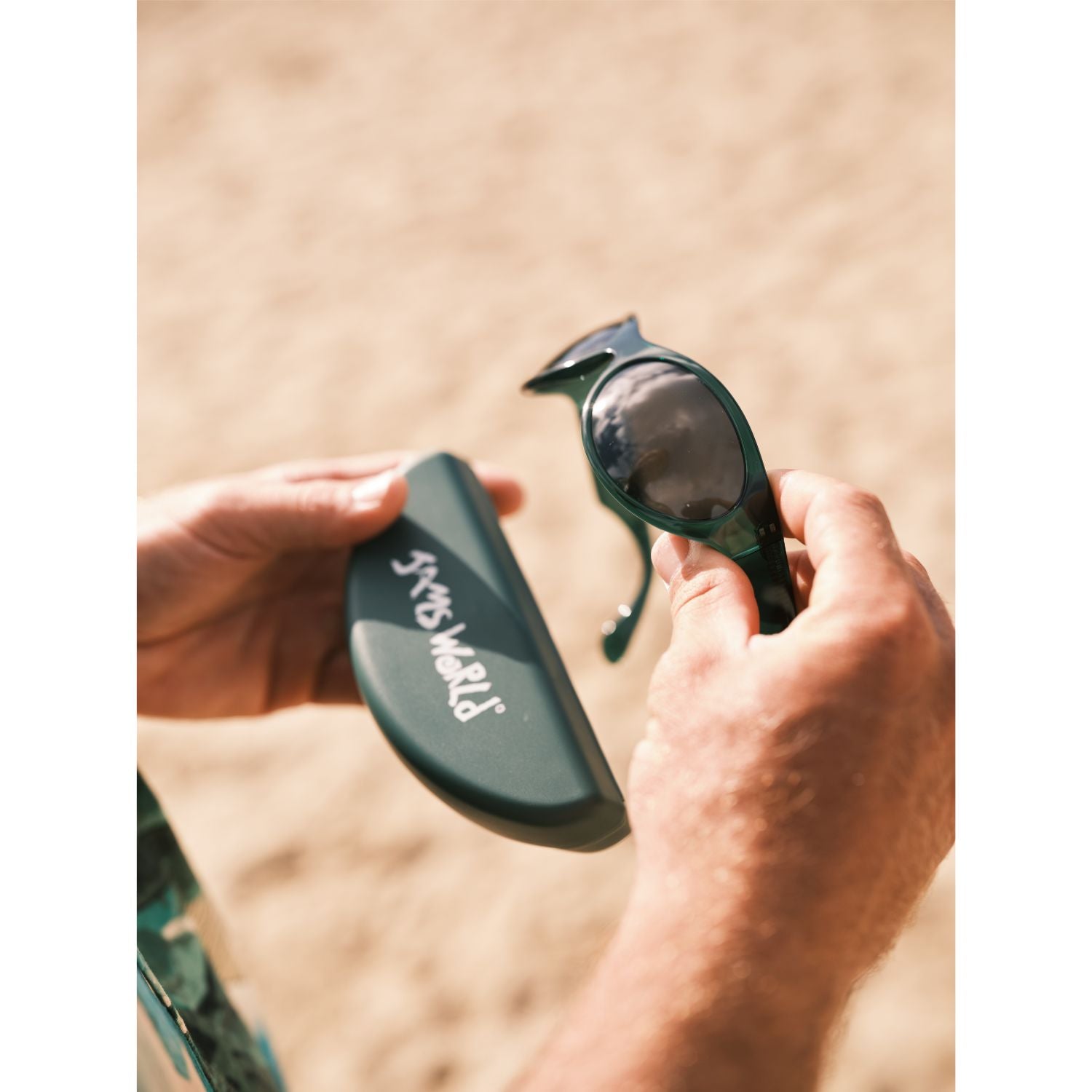 Hand holding green sunglasses with case and blurred beach background