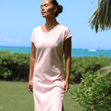 Woman in a pink dress standing outdoors with greenery and blue sky in the background