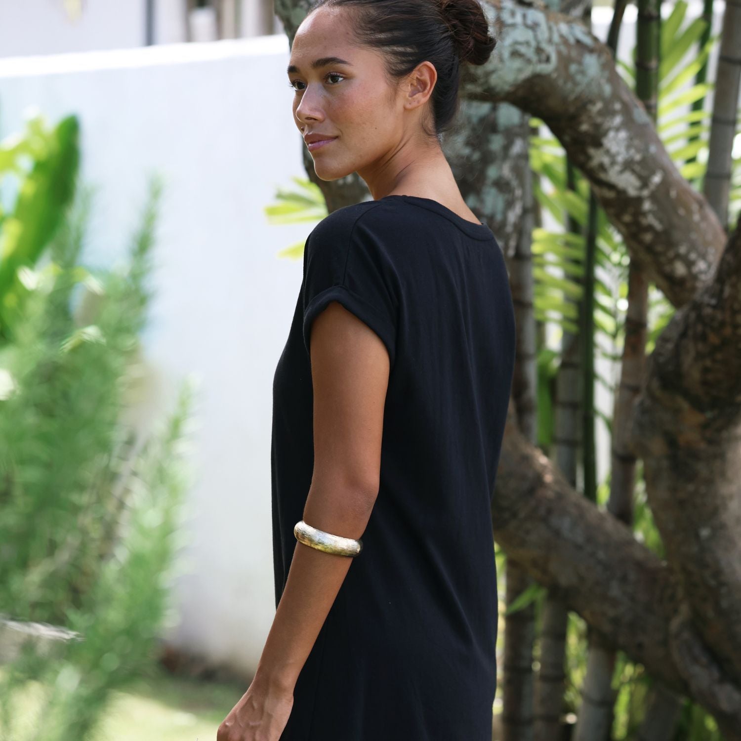 Woman in a black dress standing outdoors with greenery in the background