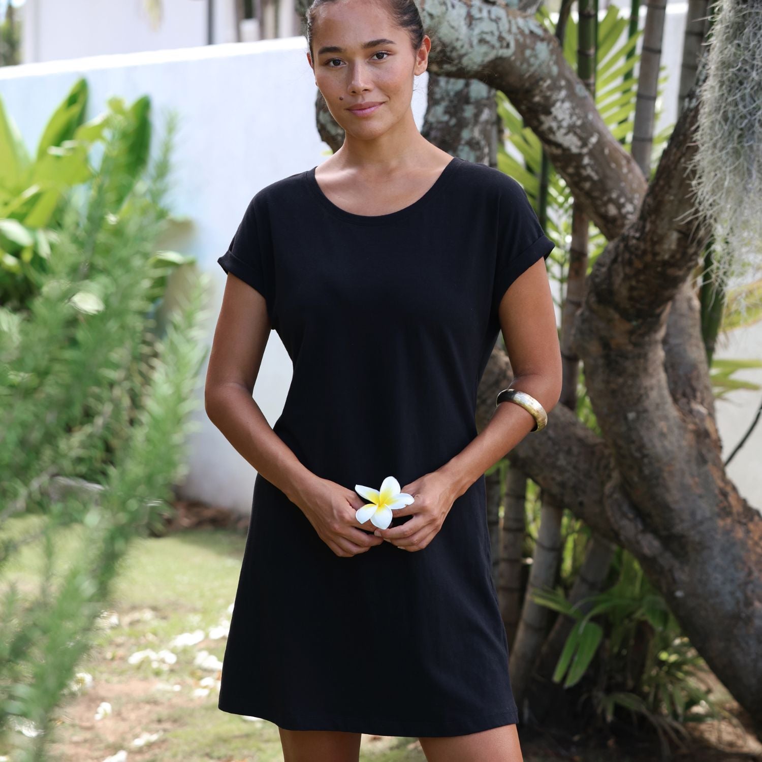 Woman in a black dress holding a white flower in a garden setting