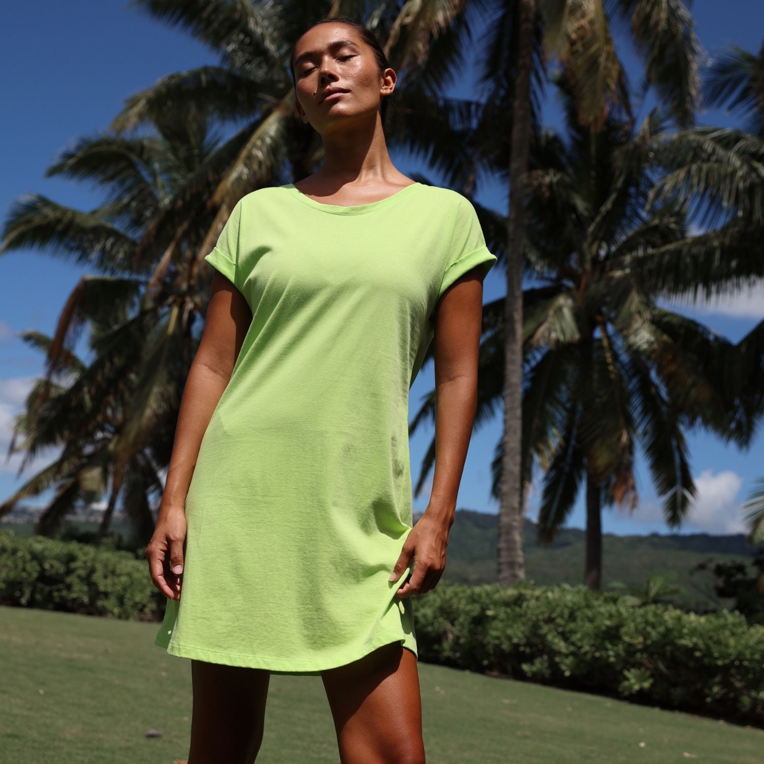 Person wearing a green dress standing in a tropical setting with palm trees.
