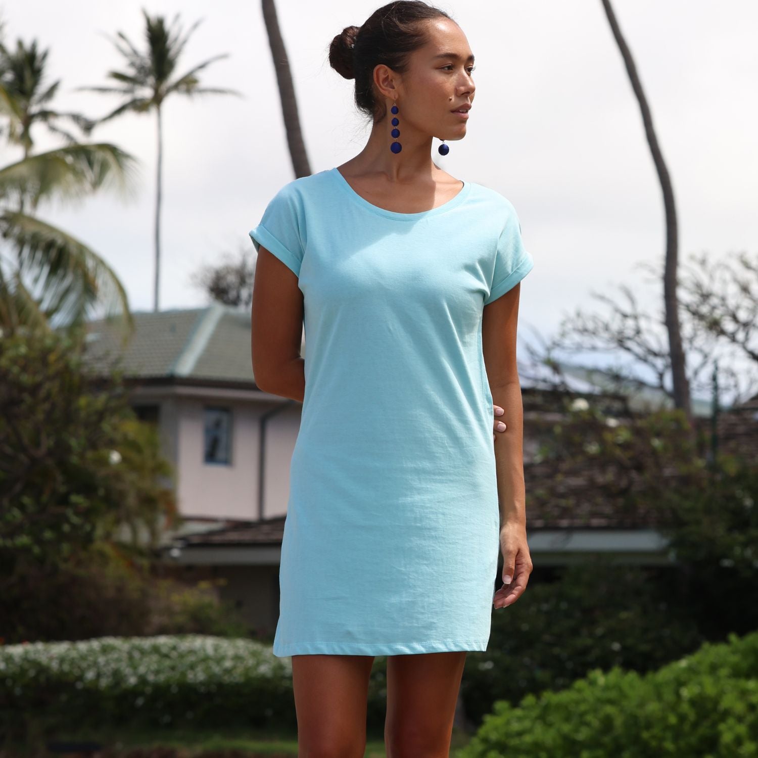 Woman wearing a light blue dress standing outdoors with greenery in the background