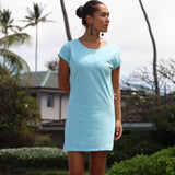 Woman wearing a light blue dress standing outdoors with greenery in the background