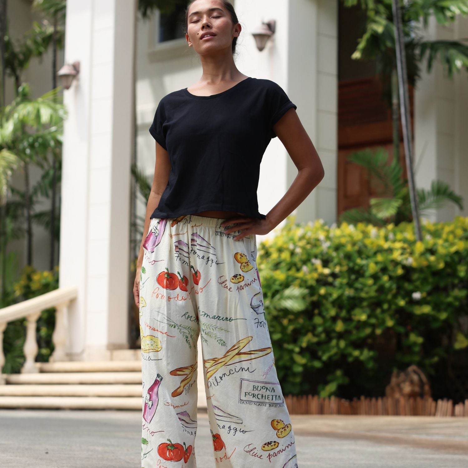 Woman wearing a black top and colorful printed pants standing outdoors.