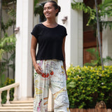 Woman wearing a black top and colorful pants standing outdoors with greenery in the background