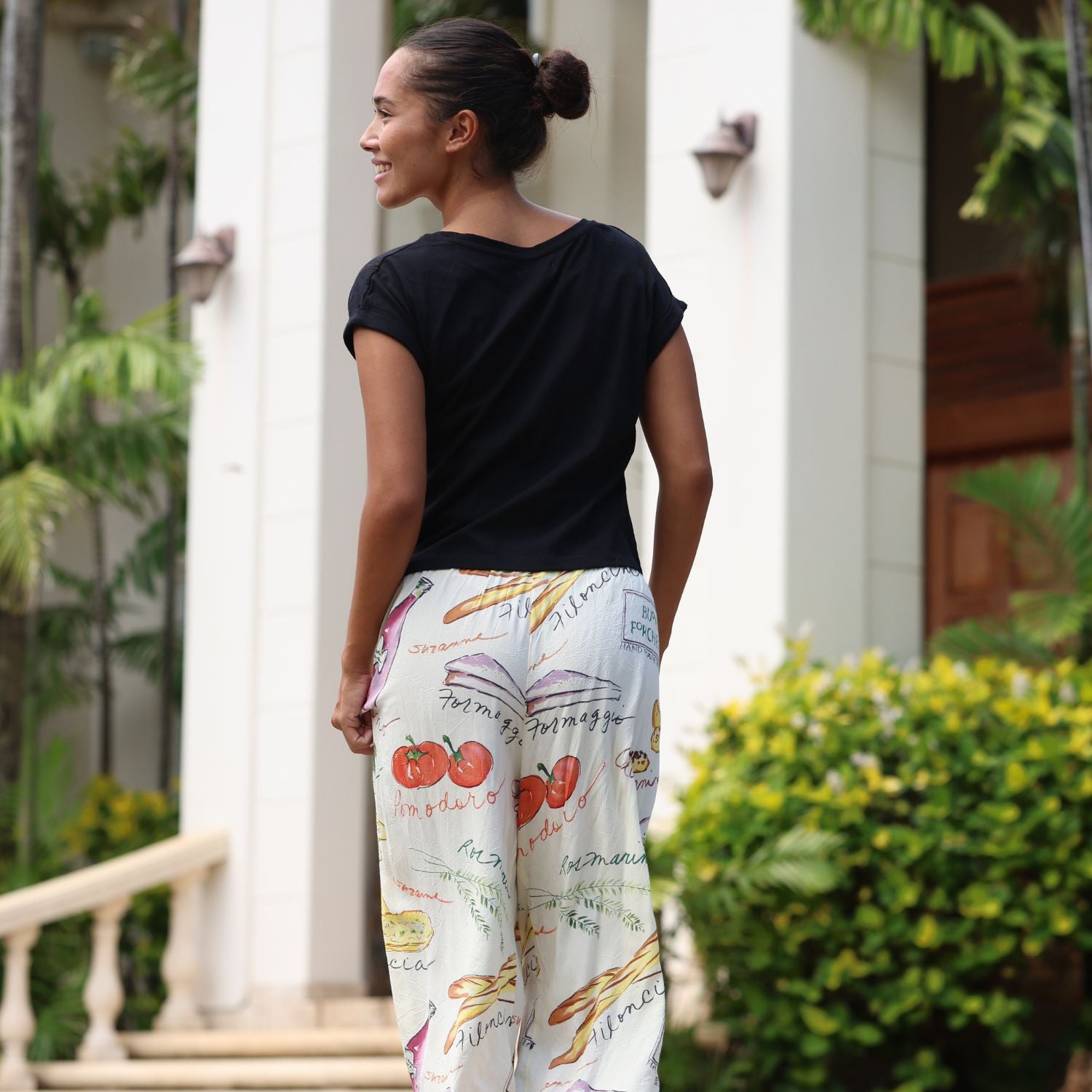 Woman wearing a black top and colorful pants with food illustrations outdoors.
