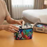 Colorful floral makeup bag with personal items on a table, with a suitcase in the background.