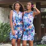 Two women modeling matching sleeveless floral mini dresses outdoors. The dresses feature a vibrant multicolor print with blue, green, red, orange, and white tones on a white base.