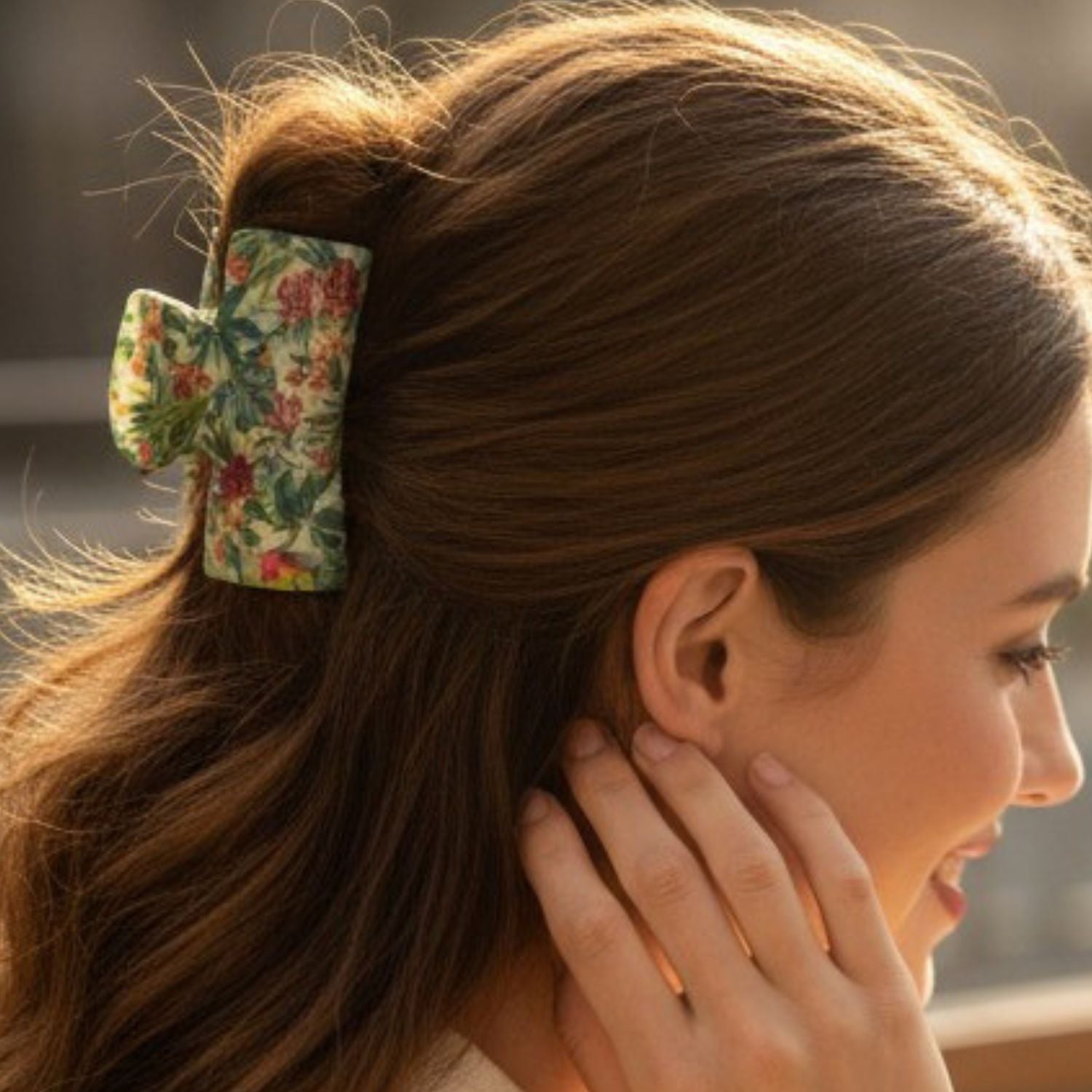 A woman with long brown hair wearing a large bow-shaped hair clip with a green, red, and yellow floral pattern, shown in a close-up side profile.