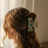 A woman shown from the side with her hair in a half-up style, secured with a fabric hair claw clip featuring a red and green floral pattern on a light background.