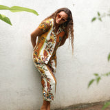 A woman wearing a matching short-sleeve button-front vest and cropped pants set with a colorful floral print, posing against a textured white wall.