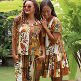 Two women wearing matching tropical batik print matching sets in an outdoor garden setting with green foliage.