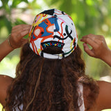 A person viewed from behind wearing a white baseball cap with a colorful abstract graffiti-style print and a black back patch that reads 'SKY WORLD'.
