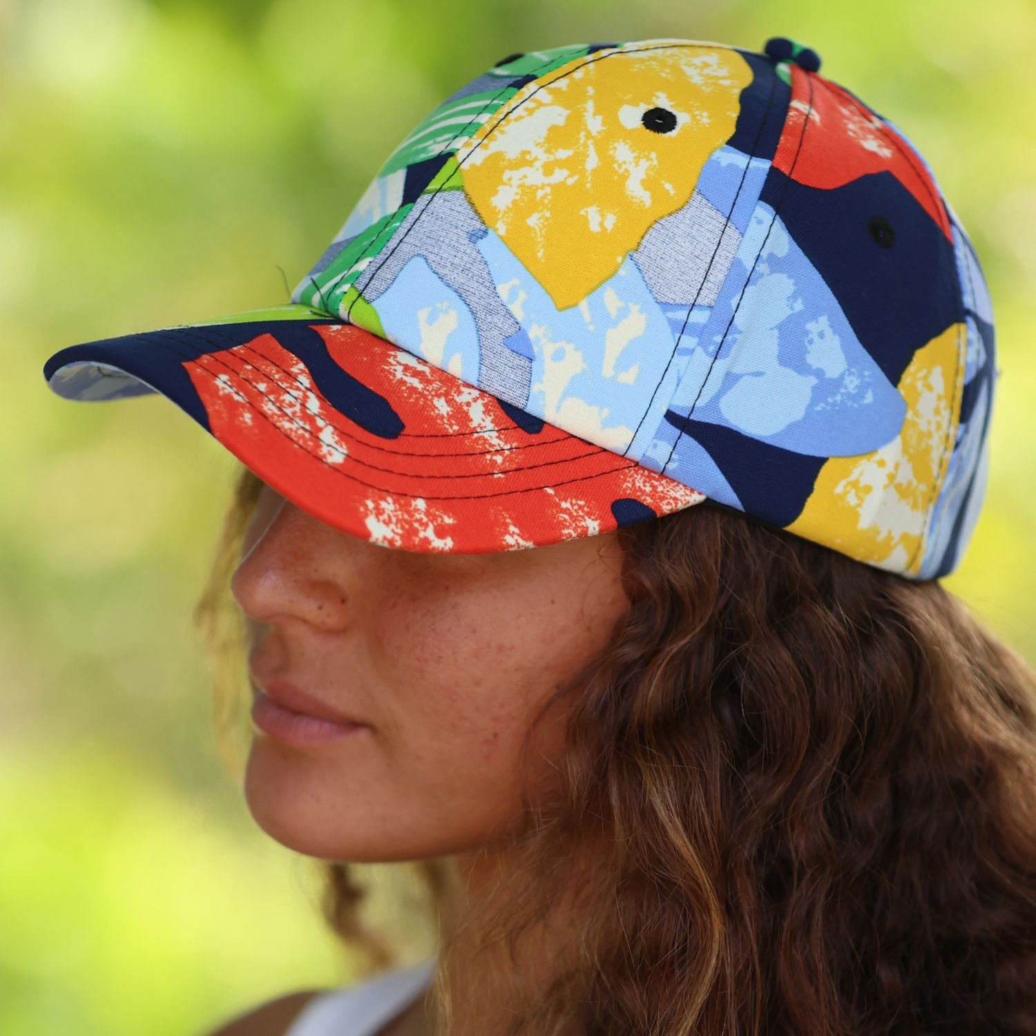 A woman in profile wearing a colorful abstract-patterned baseball cap outdoors with a blurred green background.