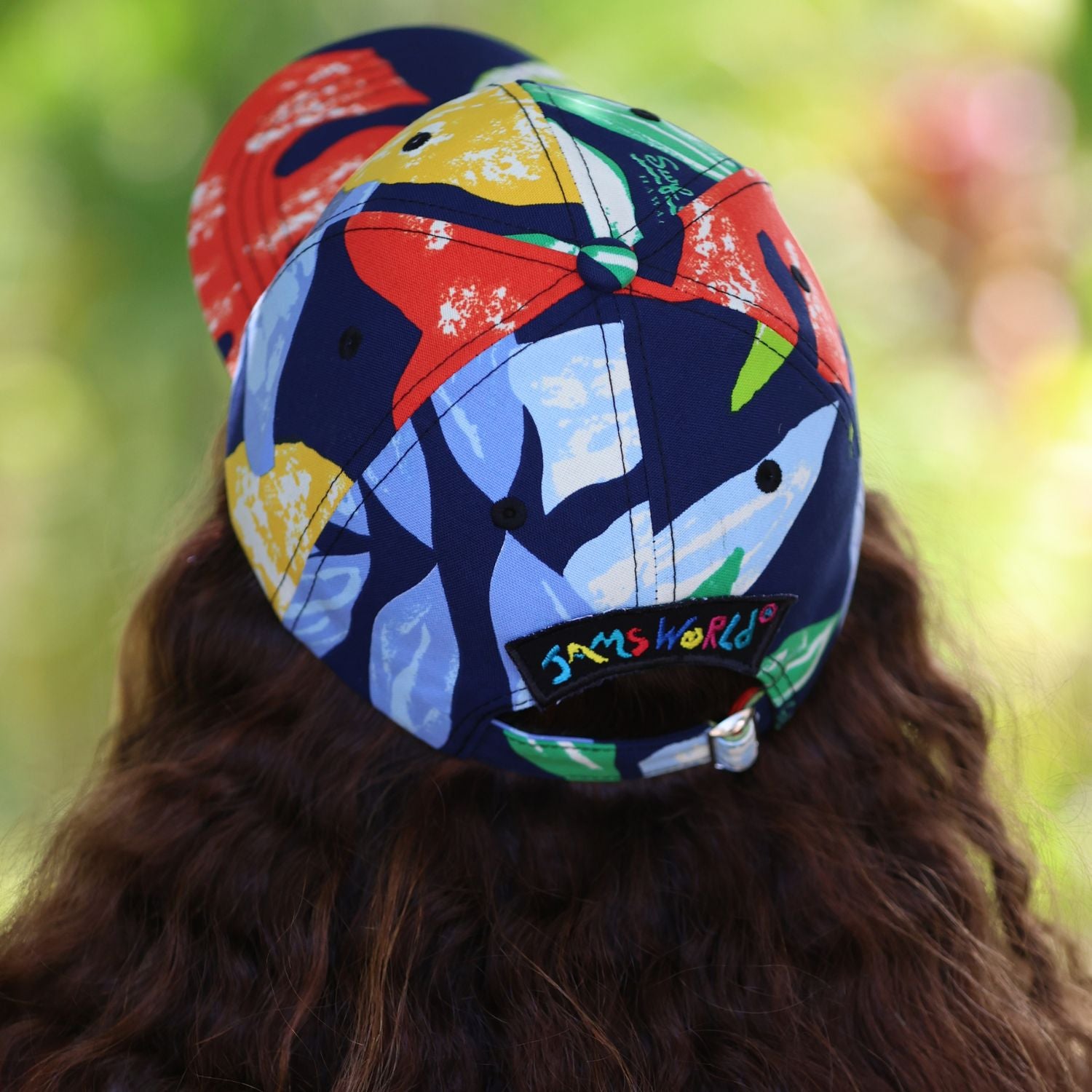 A person viewed from behind wearing a colorful patterned baseball cap with shark graphics and a visible Jamshhorld logo on the back.