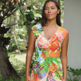 Una mujer con un colorido vestido estampado de flores tropicales, de pie al aire libre frente a un jardín borroso de fondo.