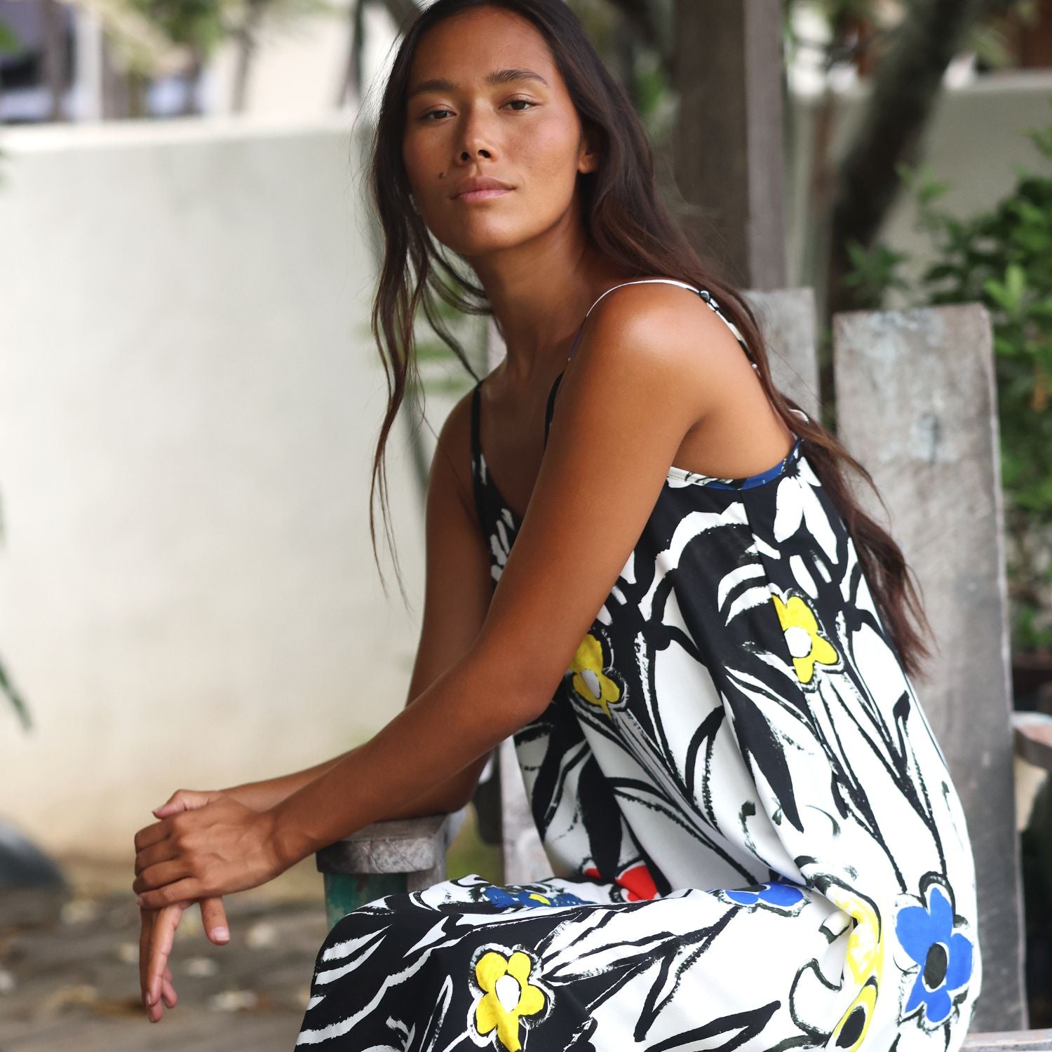 Una mujer sentada al aire libre con un vestido sin mangas de estampado floral en negro, blanco y azul con detalles amarillos.