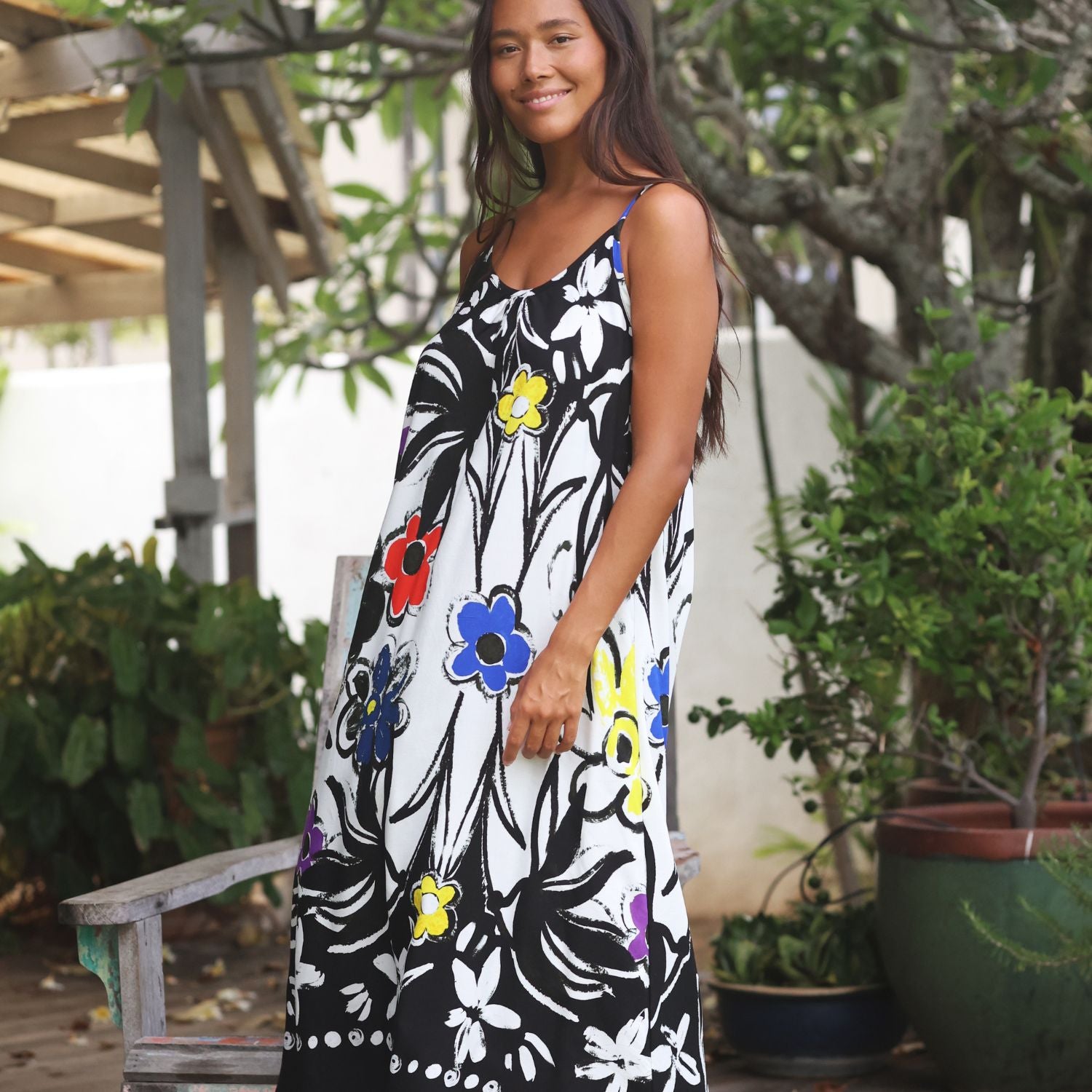 Una mujer con un vestido largo sin mangas de estampado floral en blanco y negro y colores vivos, de pie en un jardín al aire libre.