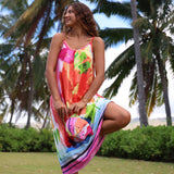 A woman wearing a vibrant, multicolored tropical print sundress stands outdoors in a park with palm trees and green grass in the background.