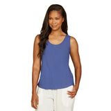 A woman modeling a sleeveless scoop-neck tank top in a medium periwinkle blue color, paired with white pants, against a plain white background.
