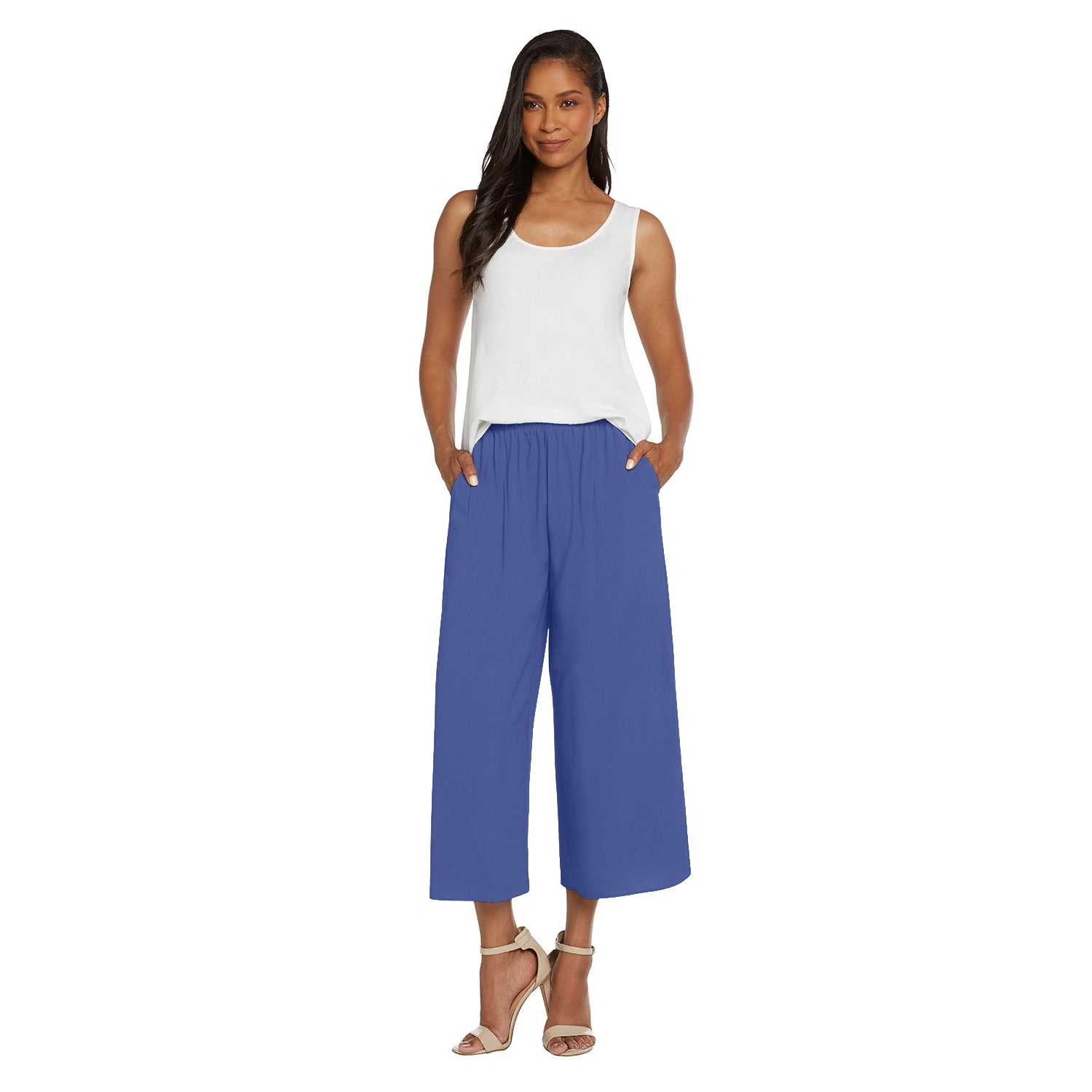 A woman modeling a pair of wide-leg cropped pants in a medium blue color, paired with a white sleeveless top and beige high-heeled sandals, against a plain white background.
