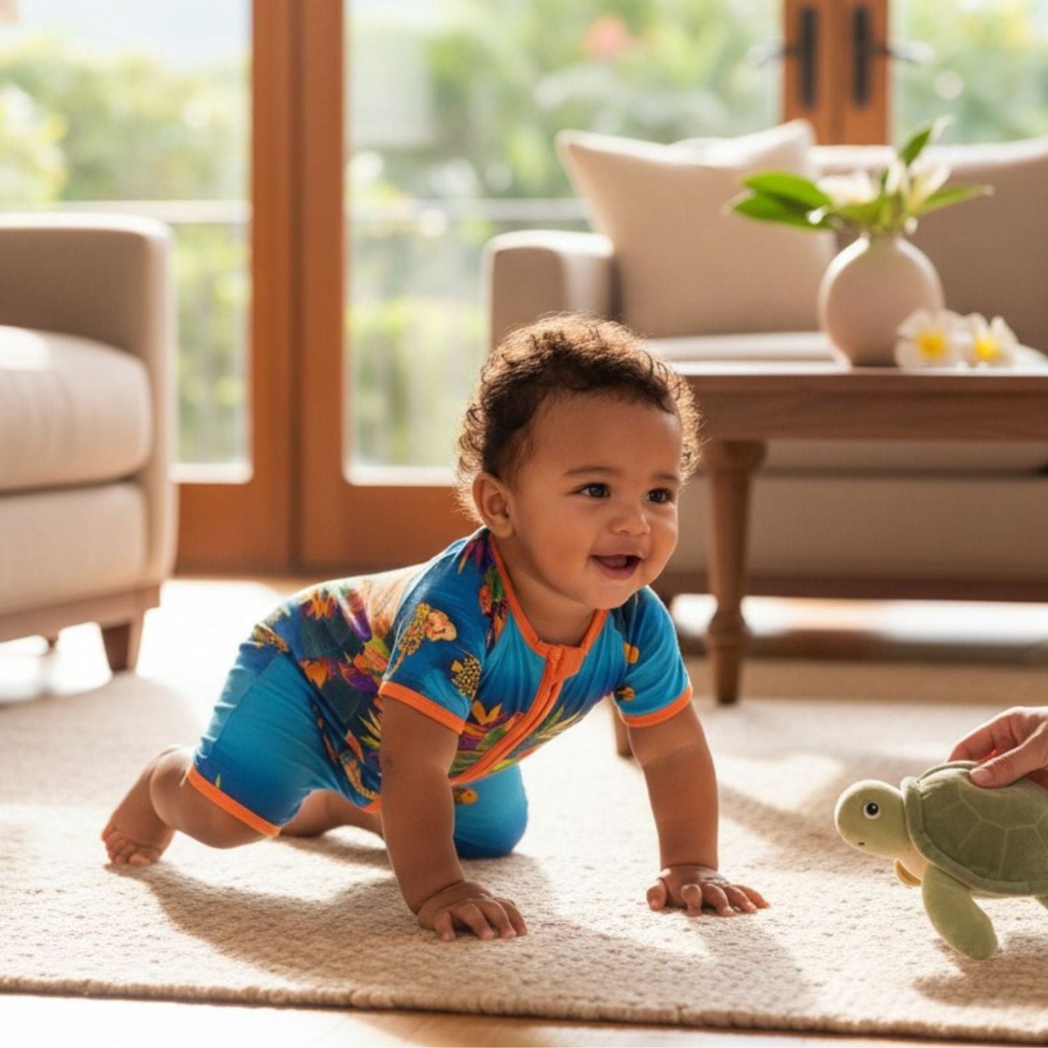 A baby crawling on a light beige rug in a bright living room, wearing a colorful blue one-piece swimsuit with butterfly and fish patterns. A hand is holding a small green turtle toy near the baby.