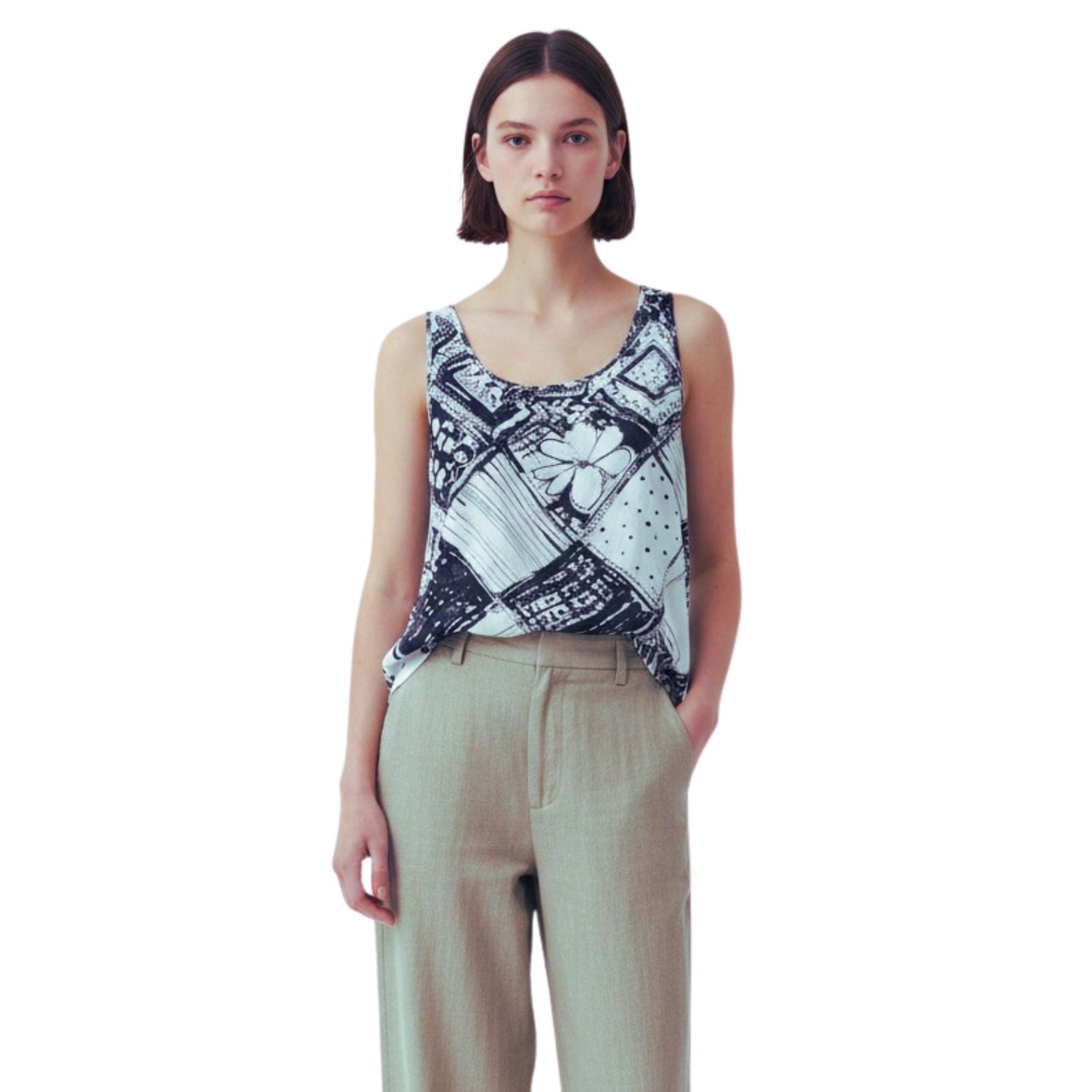 A model wearing a sleeveless scoop-neck top with a black and white graphic print, paired with light beige trousers, against a solid white background.