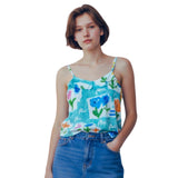 A woman modeling a light blue floral spaghetti-strap camisole top paired with blue jeans, set against a plain white background.