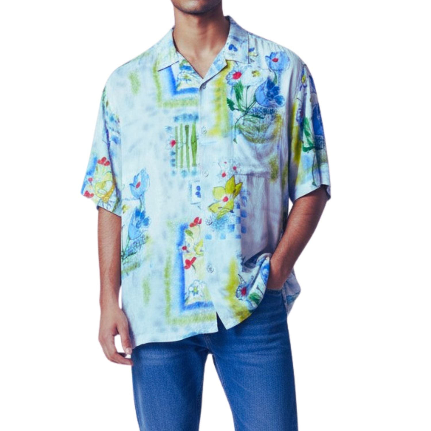 A man wearing a short-sleeve button-up shirt with a colorful abstract and floral print in blue, yellow, green, and white, paired with blue jeans against a plain white background.