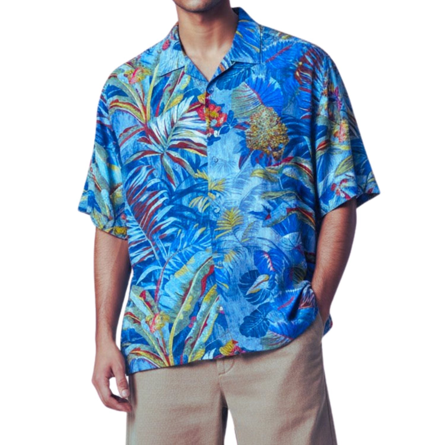 A man wearing a short-sleeve button-up Hawaiian shirt with a vibrant tropical leaf and floral print in shades of blue, red, yellow, and green, paired with khaki pants, against a plain white background.